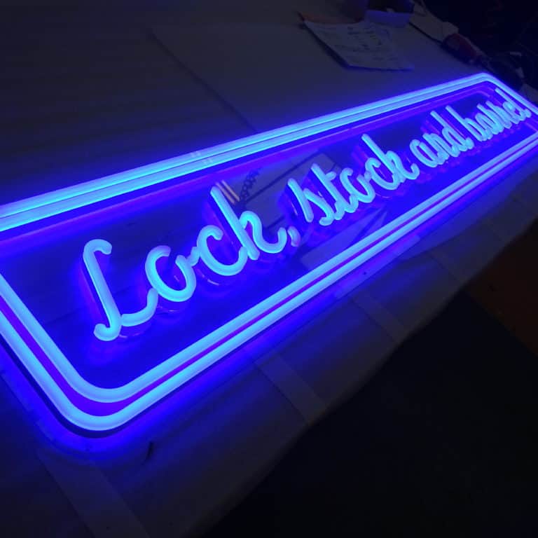 Blue faux neon bar sign with cursive script and double border, reading 'Lock, stock, and barrel' custom made by NeonPlus