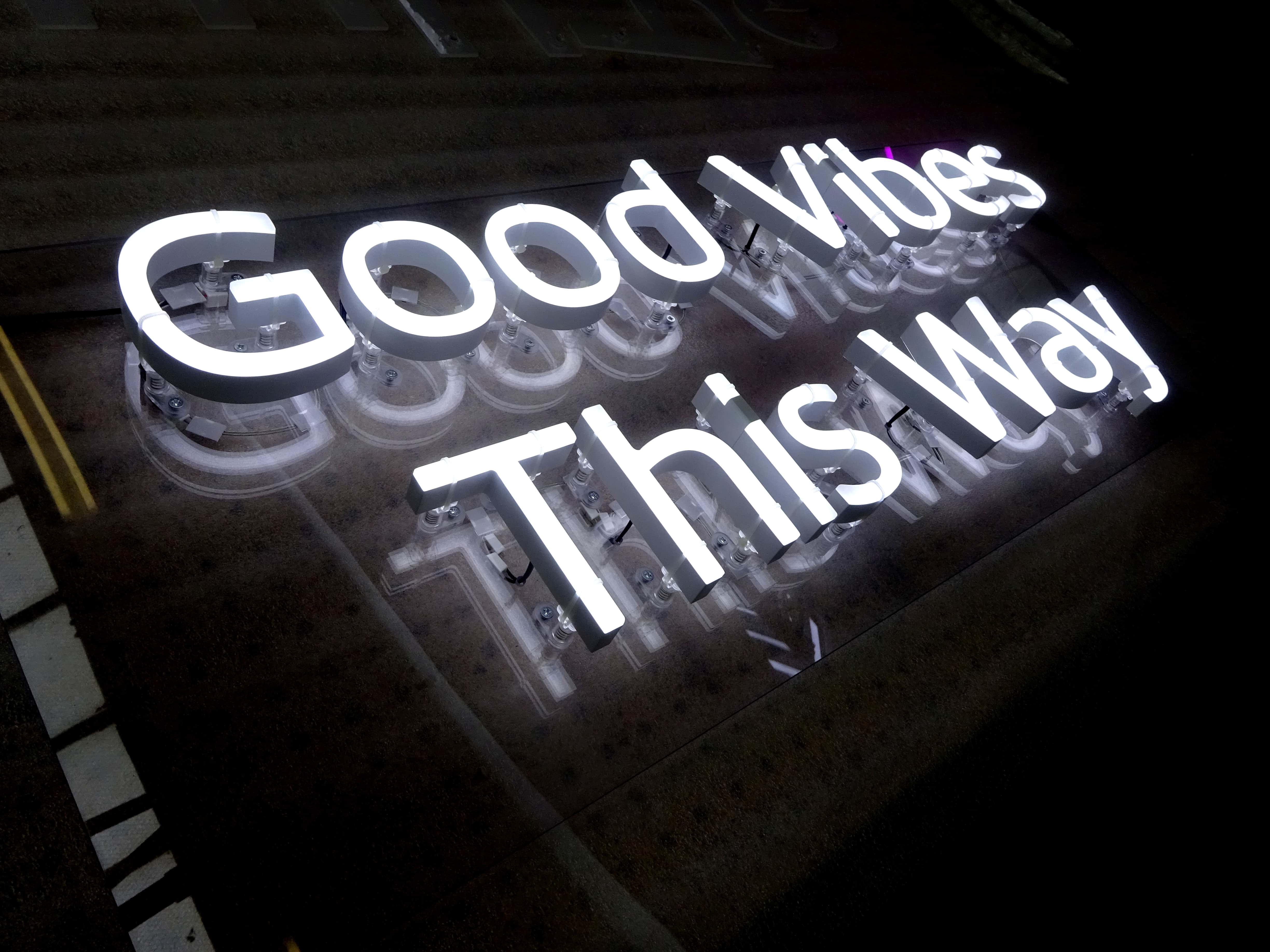 Acrylic-backed neon sign reading 'Good Vibes this Way'. Motivational neon signs for pubs and cocktail bars in energy efficient faux neon.