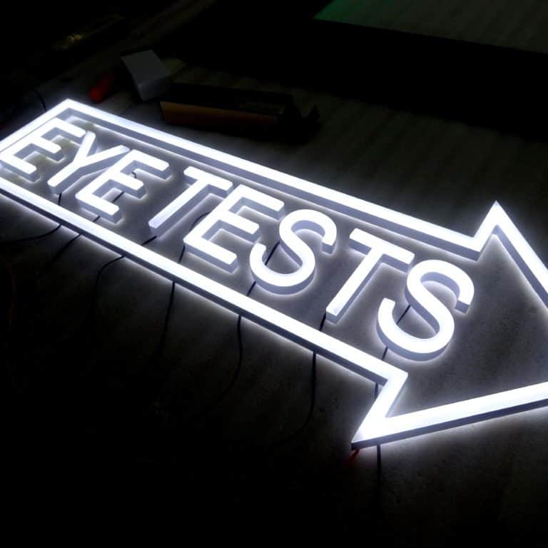 LED neon sign in white says EYE TESTS inside right pointing arrow