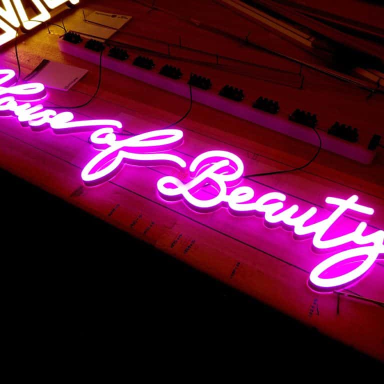 Pink neon handwriting sign using faux neon lights. Shop sign reading 'house of beauty'.