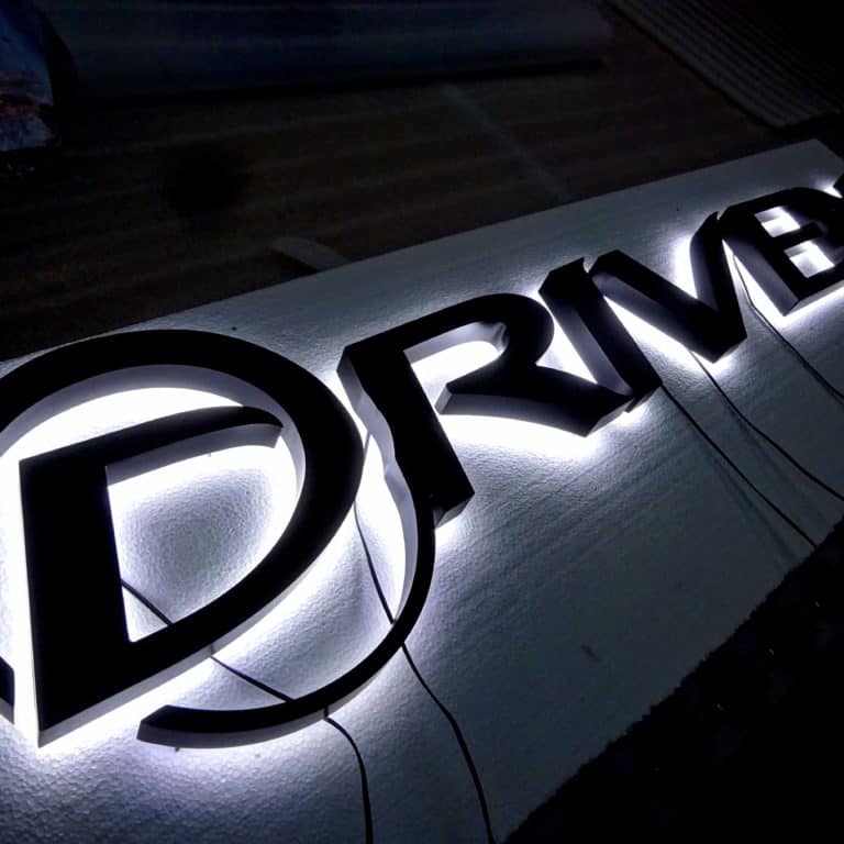 Faux neon backlit signs for businesses suitable for outdoor use. Black 'Driven' logo sign with white faux neon lights.